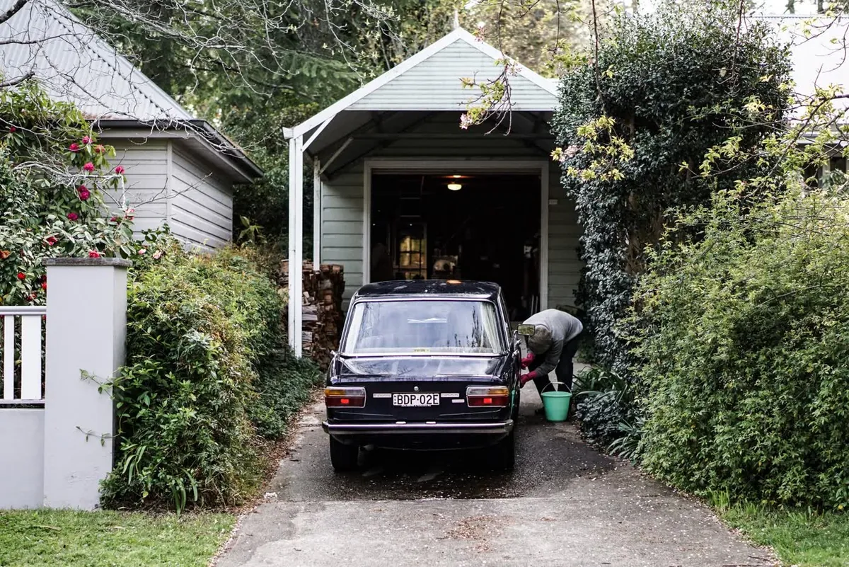 An older sedan in front of a small home garage