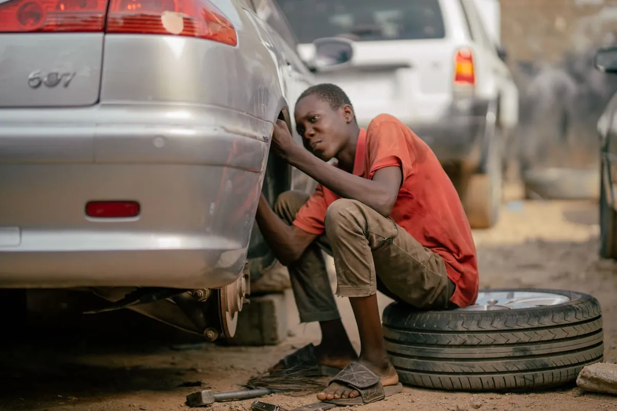 A young man sitting on a tire, working on a car wheel